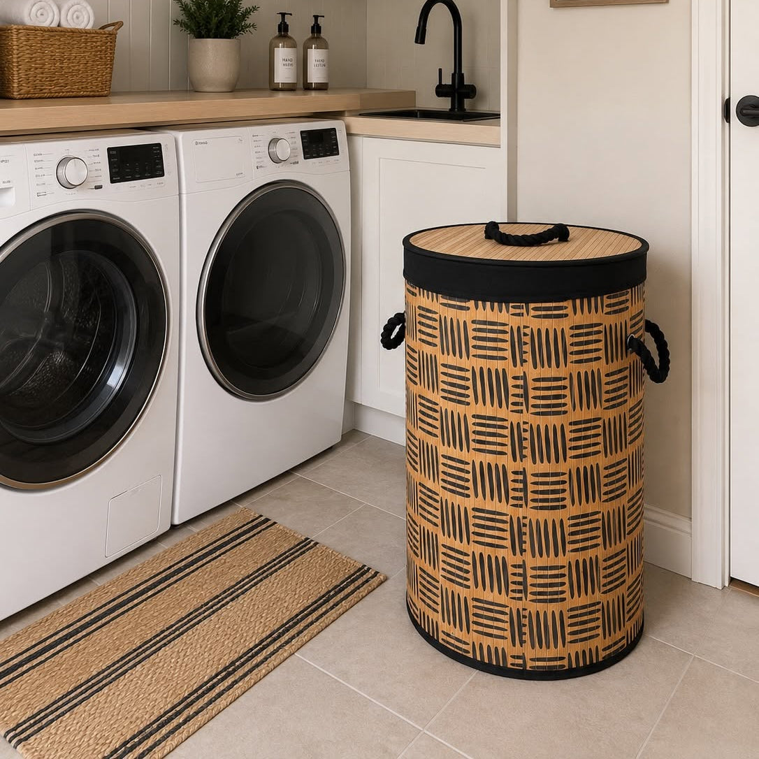 A tall cylindrical laundry hamper with a black and tan woven basket pattern and black handles, placed in a bright, modern laundry room next to a washing machine and dryer.